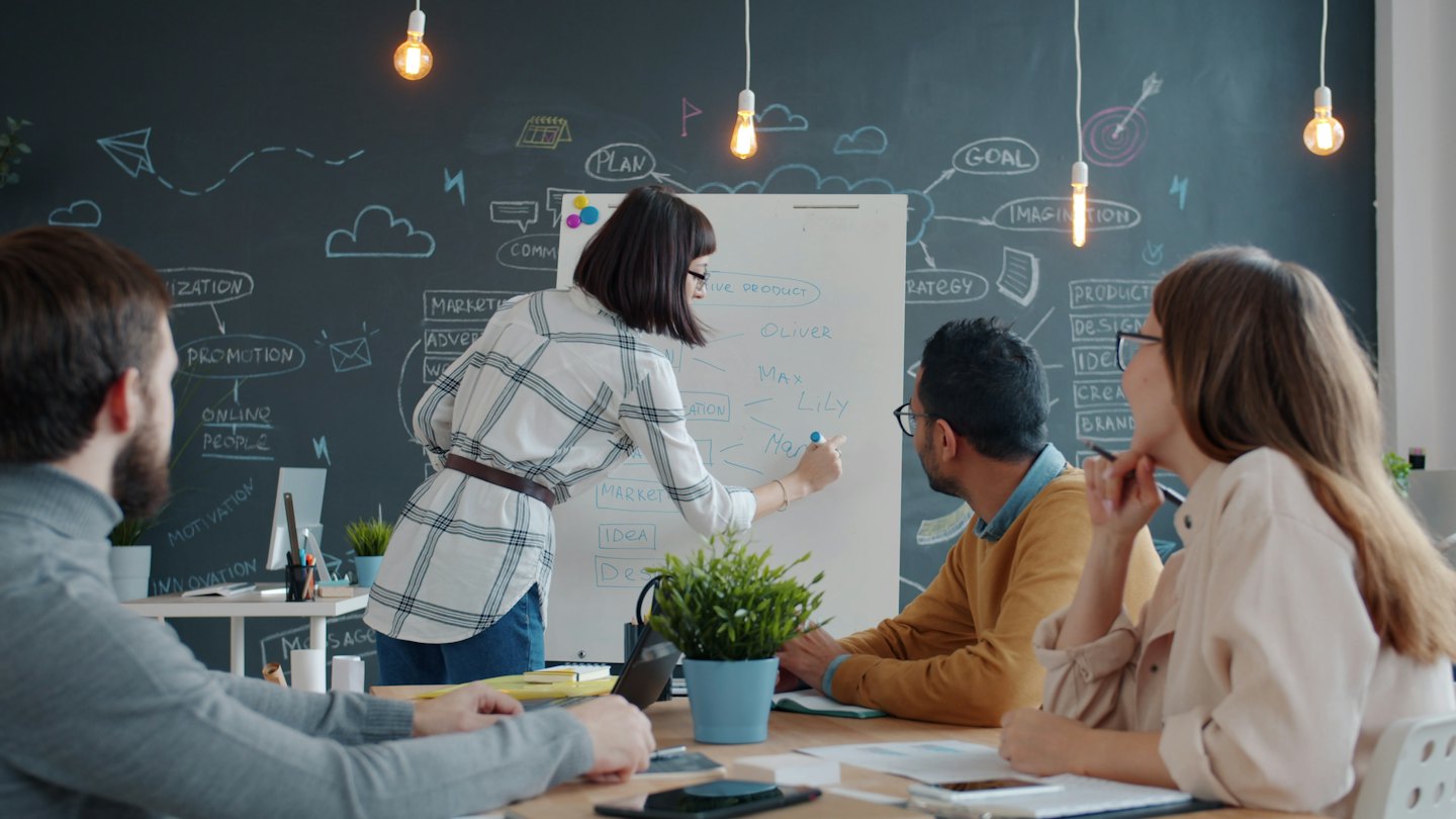 Professionals brainstorm ideas on a whiteboard in a modern office.